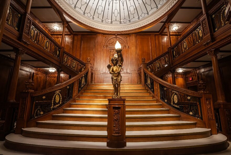 A full-size replica of the grand staircase on the Titanic, with a central wide staircase branching off on both sides with ornate carved wooden balustrades and a domed ceiling.