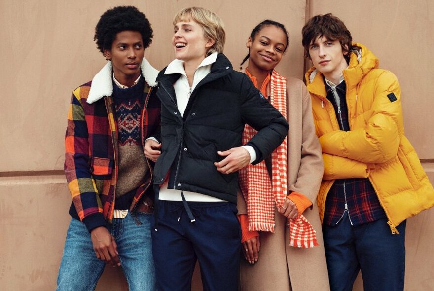 Four models leaning against a wall wearing winter coats with bright colours