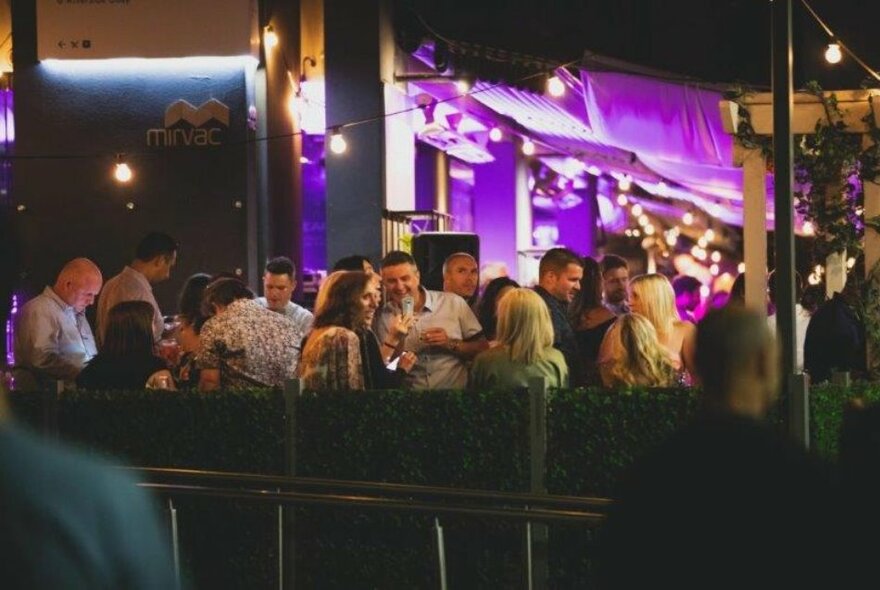 People seated at outdoor tables at night with purple lights.
