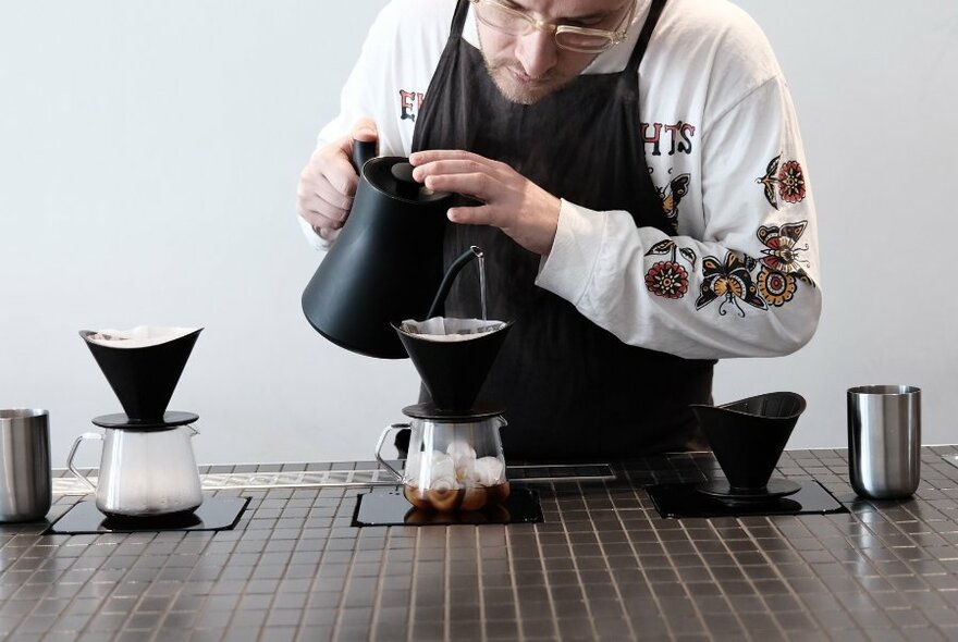 A barista pouring coffee through a filter over ice 