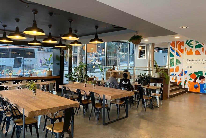 Bright interior cafe space, with large communal tables, windows facing the street, and steps leading down from the front entrance.