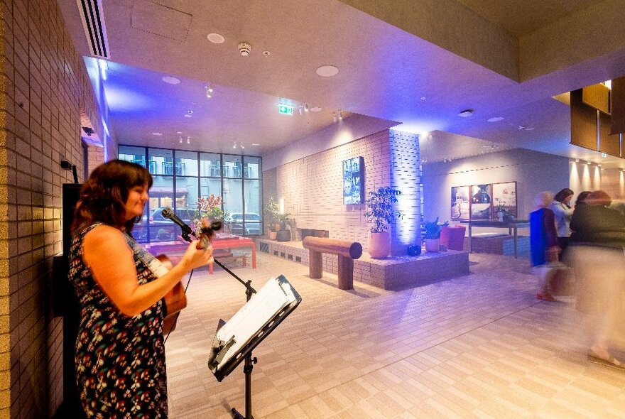 A solo singer with a guitar performing in an empty lobby space.