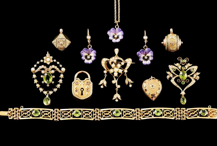 Black background with antique jewellery display including peridot and gold bracelet, violet flower earrings and lock charm.