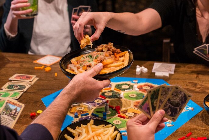 People playing board games while handling loaded fries. 