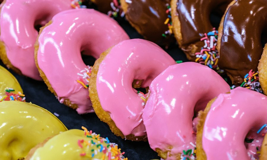 Rows of yellow, pink and brown doughnuts with sprinkles.