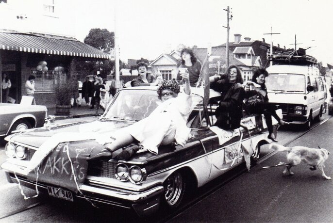Black and white of vintage car, with people atop, in a car procession.