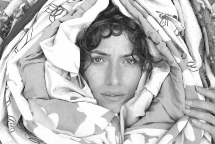 The face of singer Aldous Harding surrounded by layers of fabric, as if cocooned; black and white photo.