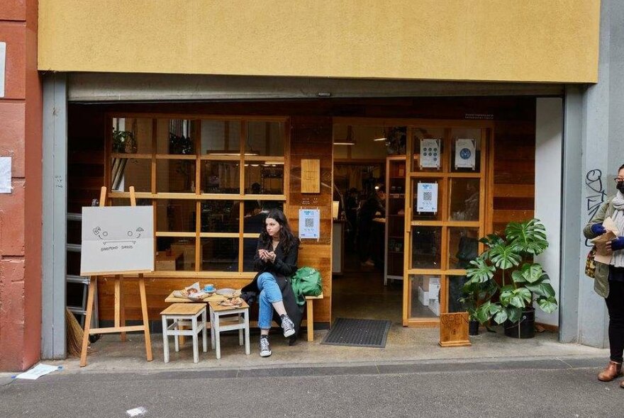 A woman sitting outside a cafe in a laneway