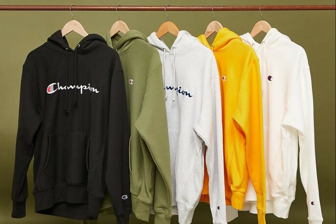 Row of black, green, white, yellow and white Champion hoodies hanging on a rack.