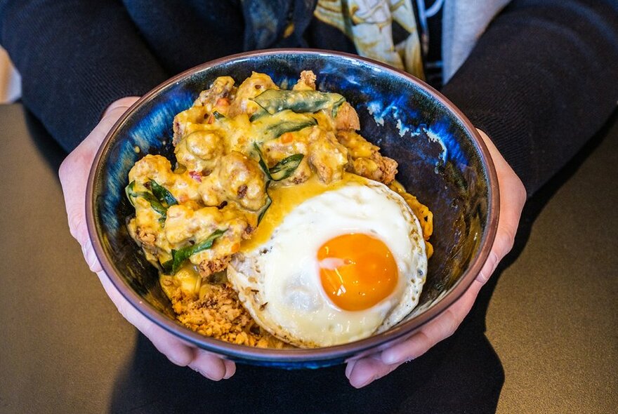 Someone holding a bowl of Indonesian food with a fried egg on top.