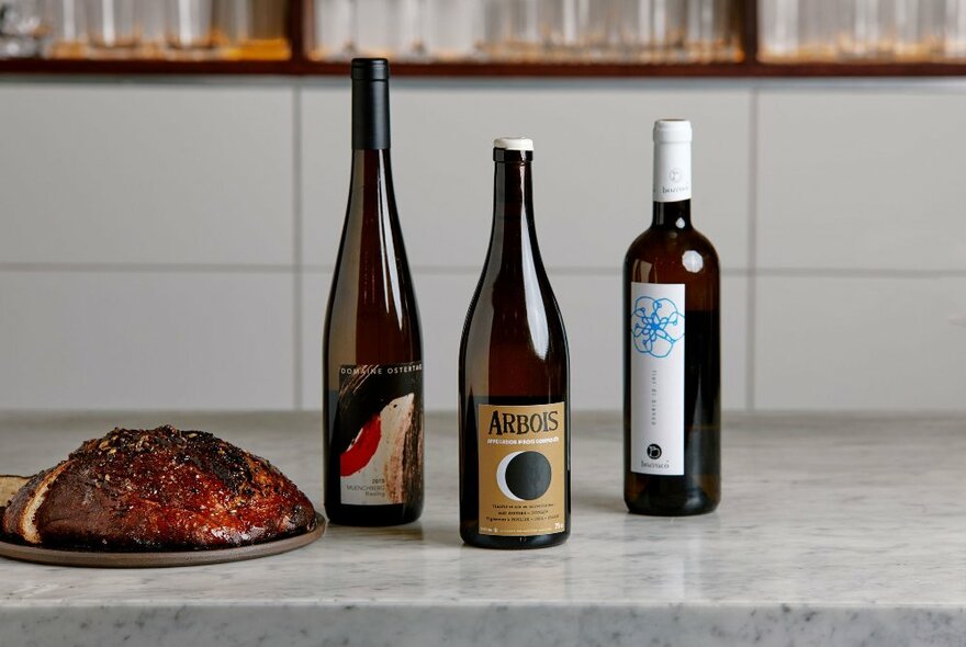 A marble benchtop with three bottles of wine and a roasted meat dish.