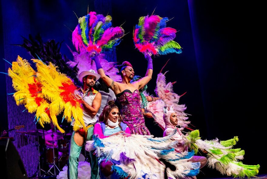 Four drag perfomers on stage in brightly coloured costumes with feather fans.