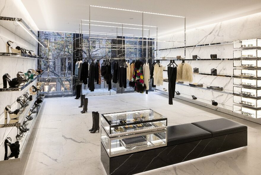 A black and white marble shop interior with shoes lining the walls and clothing hanging from a rail in the centre 