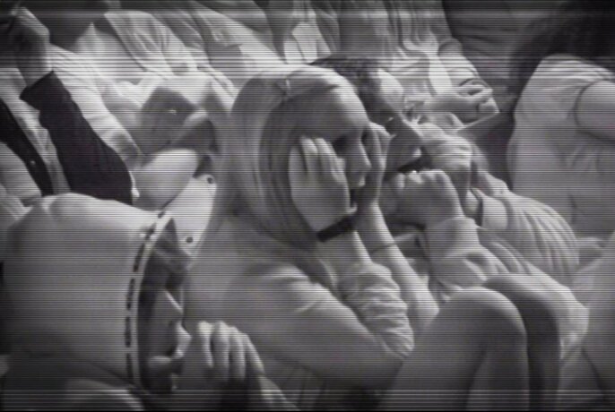 Black and white image of audience members watching something and looking scared with hands covering their eyes.