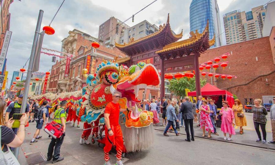 A parade of performers walking a long lion puppet down a street during Chinese Lunar New Year