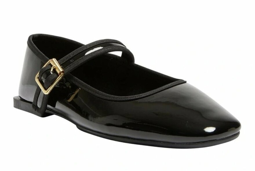 A patent black flat shoe with a gold buckle on the strap.