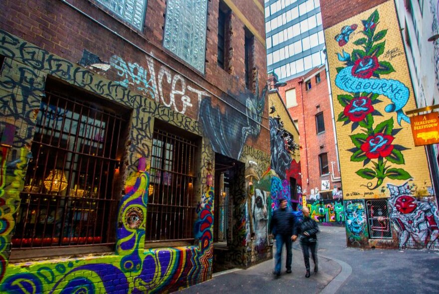 Two people walking through a laneway covered in street art.