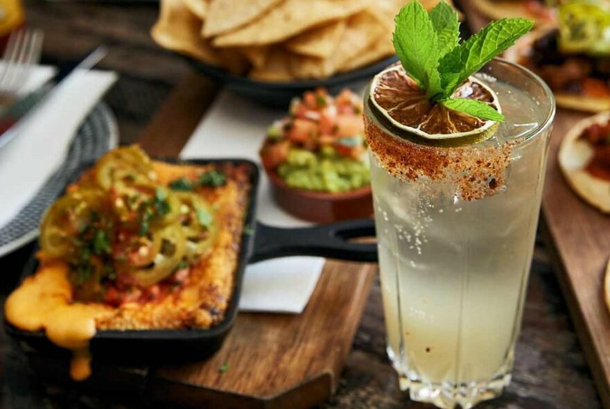 A skillet filled with Mexican food beside a cocktail