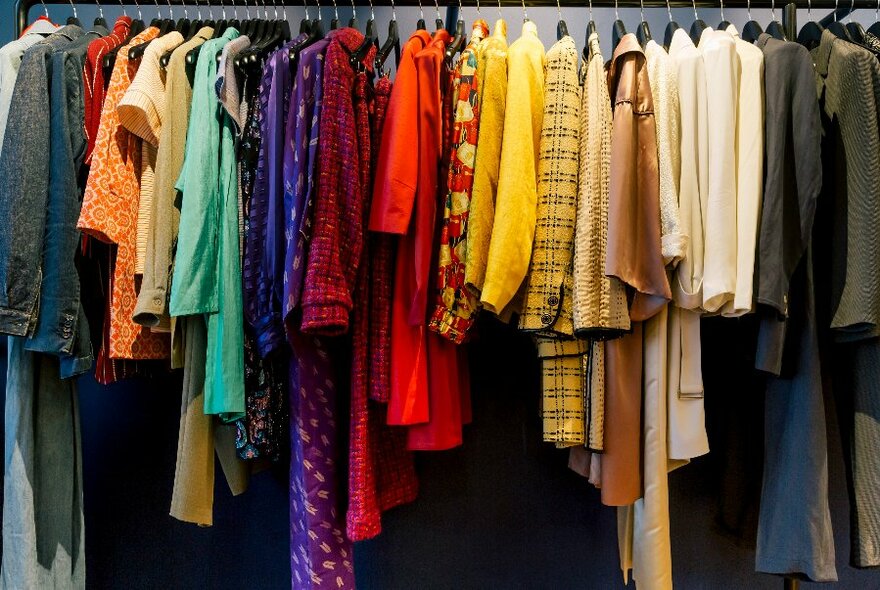 Brightly coloured vintage dresses and designer clothes hanging on racks against a dark wall.