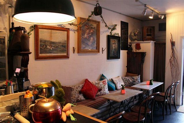 Cosy wine bar interior with pendant lighting, bench with cushions and paintings on the wall.