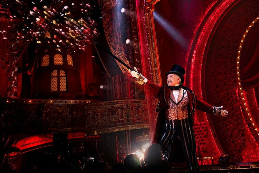Showman in top hat on red stage, holding cane up into to the air.