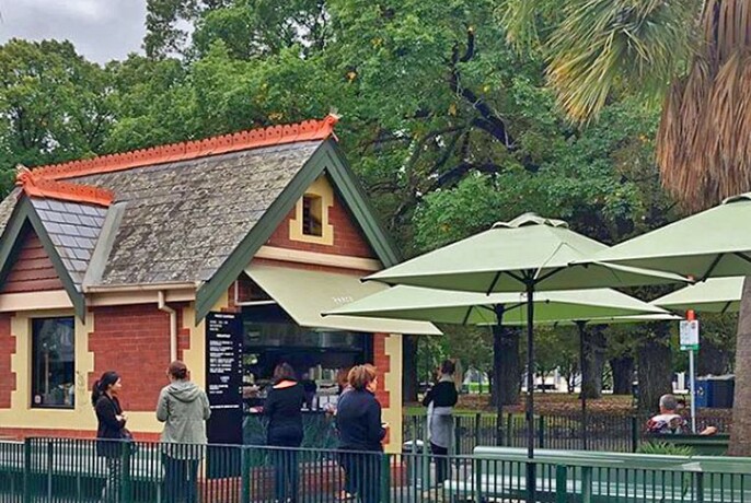 Cute little cafe built in heritage-style cream and red brick, with slate roof and green shade umbrellas outside..