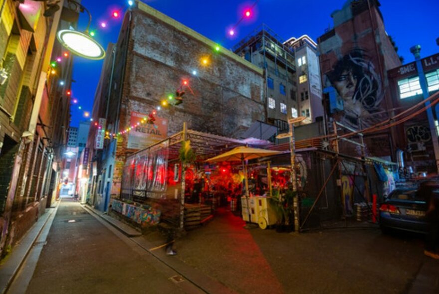 Night time wide shot of laneway brick bar with fairy lights and neon lights. 