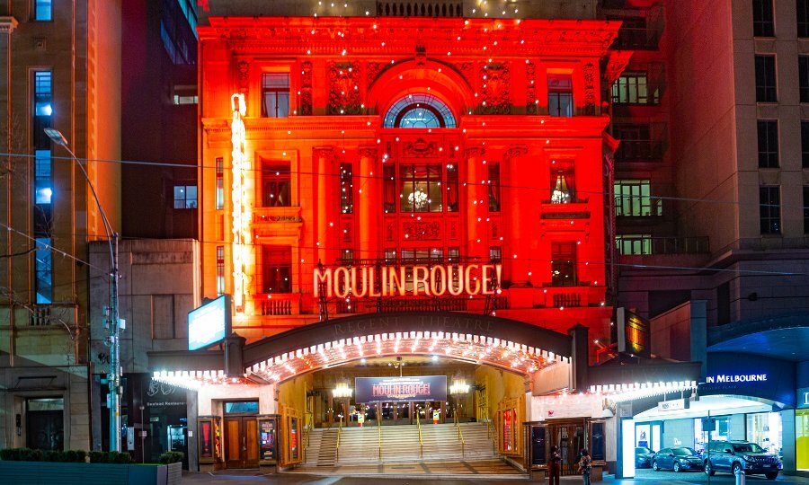 The exterior of a theatre lit up red for Moulin Rouge. 