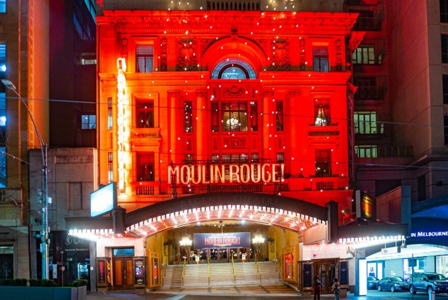 The exterior of a theatre lit up red for Moulin Rouge. 