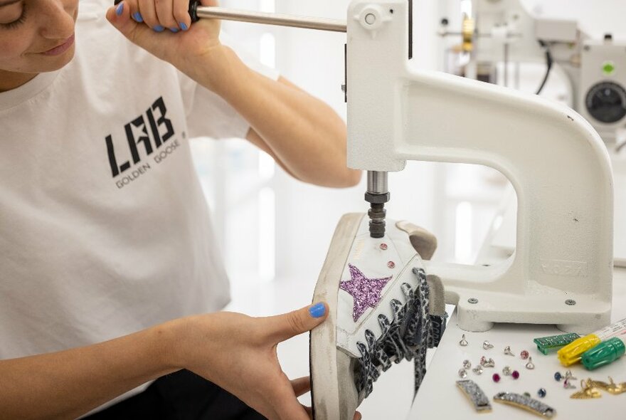 A woman applying embellishments to a pair of white sneakers with a press machine