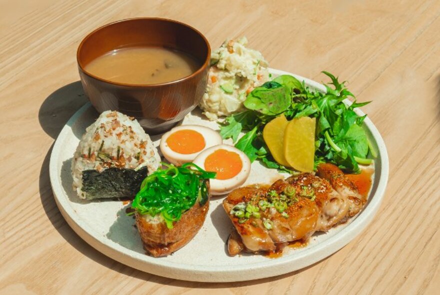 A selection of Japanese food items including miso soup and pickled eggs on a round, white platter on a wooden table.