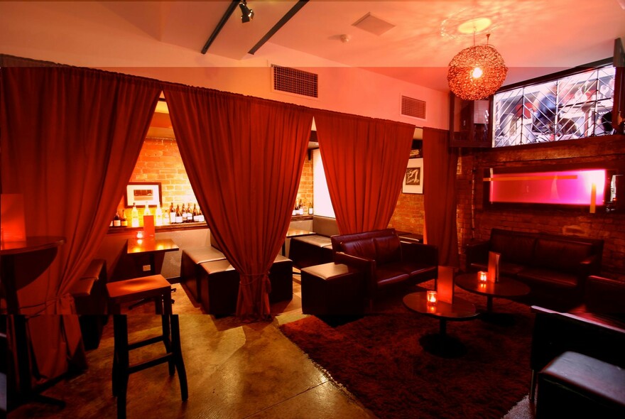 Intimate bar split into two areas by a line of red curtains, with red candles on tables.