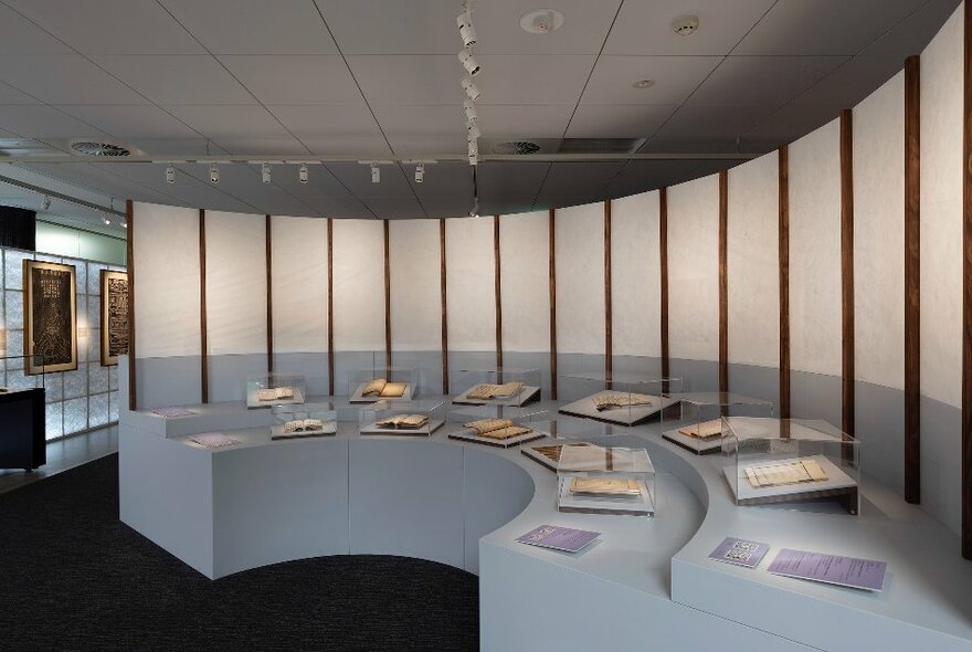 An exhibition space with manuscripts on display on a curved bench with transparent screens.