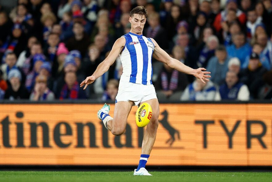 North Melbourne AFL football player kicking a yellow ball during a match.
