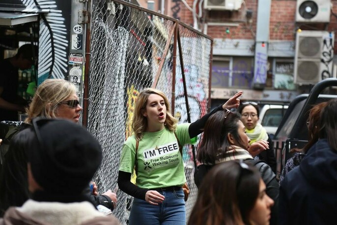 Tour guide pointing and talking to a group of people in a city laneway.