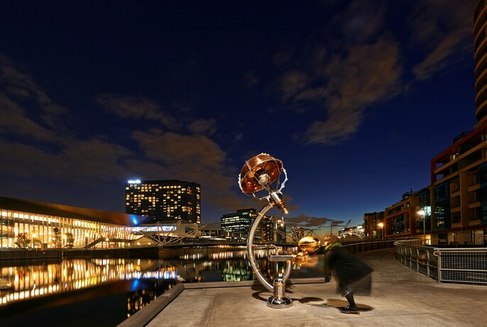 Sculptural artwork of bronze, steel and copper with lit-up buildings in the background.