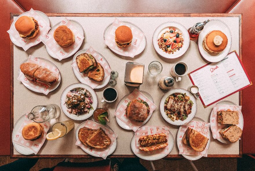 Overhead shot of a table loaded with dishes and drinks including coffees, pancakes, toast and burgers.