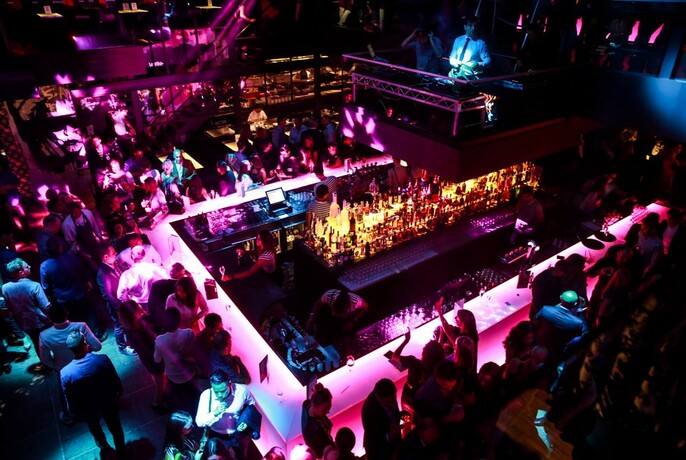 Overhead view of the large central bar at Ms Collins, crowded with people, and with the DJ booth visible on the level above.