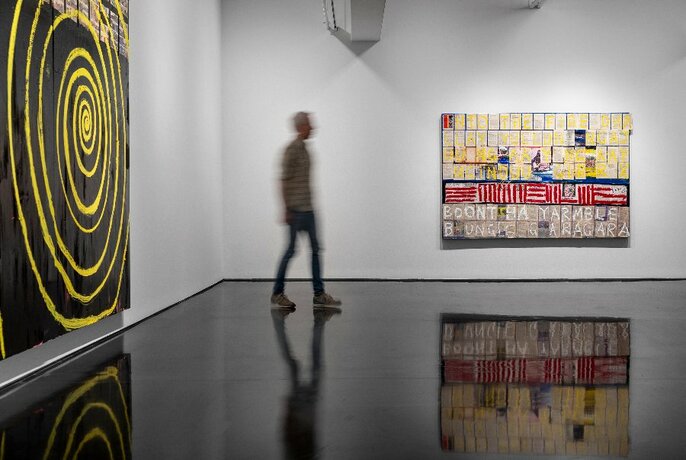 Person walking through a gallery with large paintings.