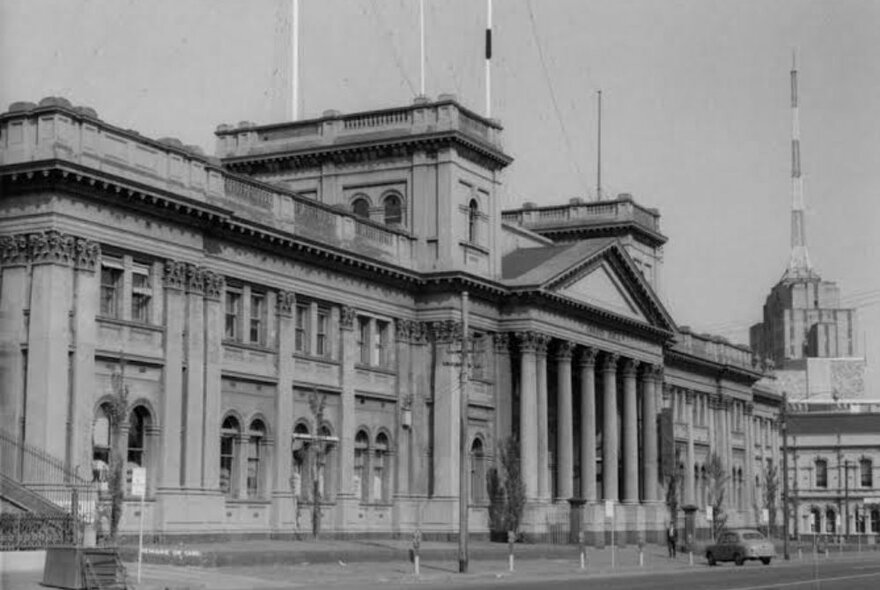 Black and white image of Trades Hall Council building facade with Russell Street Police Station and spire in the background.