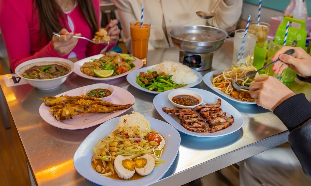 People dining on shared Thai dishes on colourful plates on a silver restaurant table.