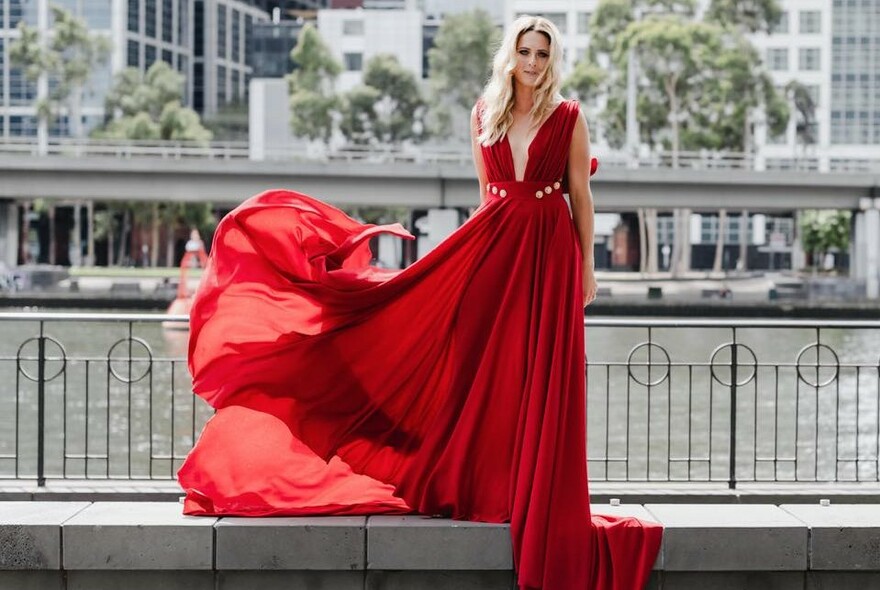 Model in voluminous red dress standing riverside.