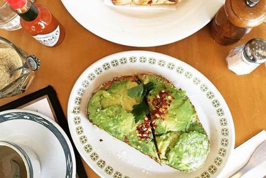 Table setting with avocado on toast and condiments.