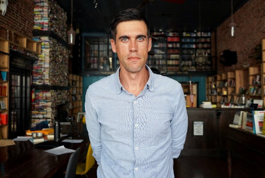 American author Ryan Holiday standing in a library crowded with books.