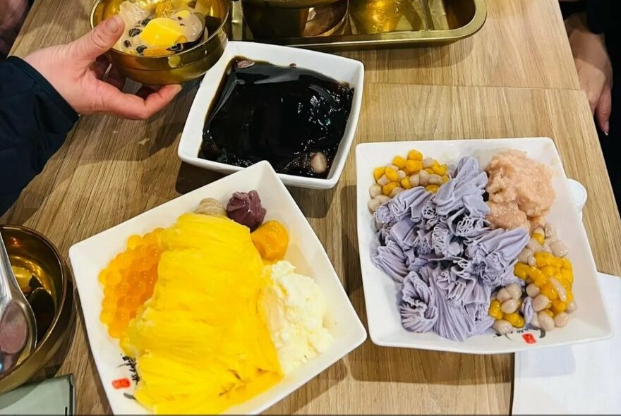 Table with dishes of Taiwanese desserts including purple ice cream and yellow custard.