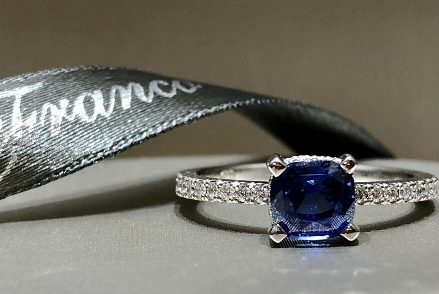 Grey branded ribbon with diamond and sapphire platinum ring.