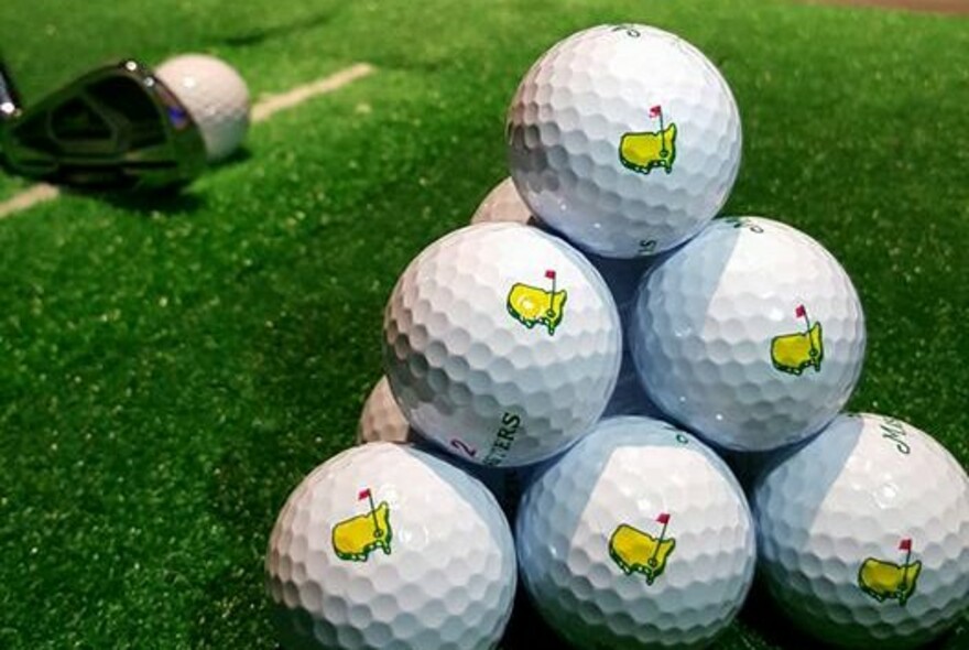 Pyramid stack of white golfs balls on green turf with a golf club in the background.