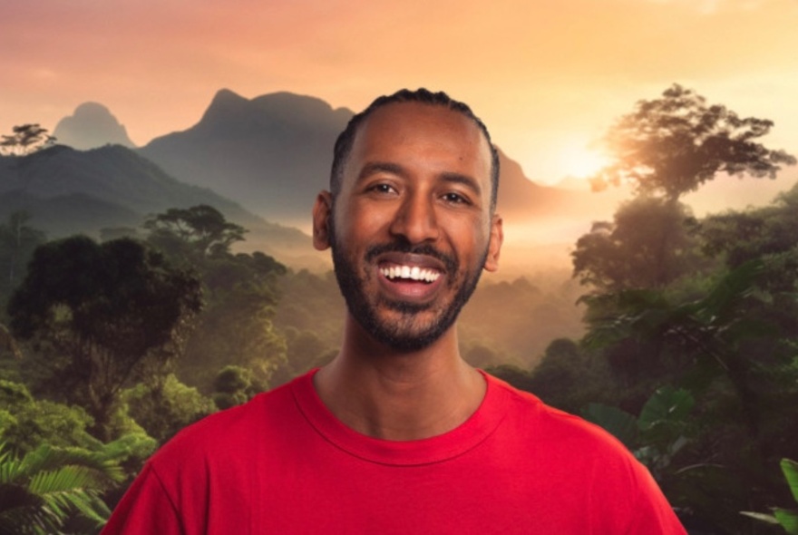 Comedian Samuel Gebreselassie, smiling in front of a landscape of mist-shrouded hills and trees, wearing a red T-shirt.