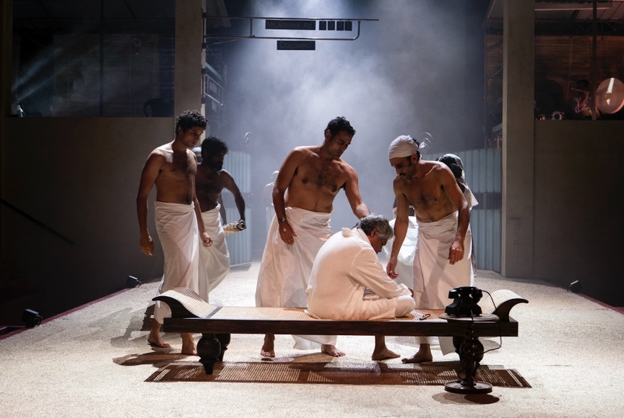 Men wearing white towels in a sauna, one seated on a bench wearing a white robe.