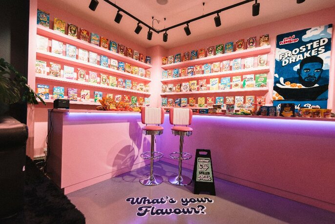Candy pink cereal bar: two corner wall with cereal packets on display, bar and two stools facing out. 